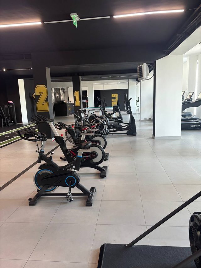 Rząd rowerów spinningowych i orbitreków w strefie cardio, w tle numery stref na słupach