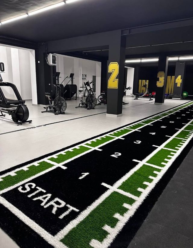 Tor sprinterski z linią startu i oznaczeniami metrów, w tle strefa cardio